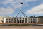 A high-resolution photograph of the Australian Parliament House in Canberra with the national flag flying, representing democracy and human rights in Australia.