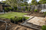 Australian backyard undergoing residential landscaping with new turf, paving, garden beds, irrigation and potted plants.